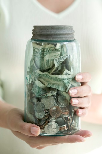 Woman holding a jar of coins and dollar bills